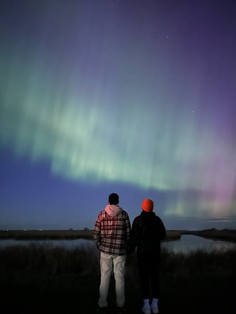 A couple stands together gazing at the aurora borealis illuminating the night sky.