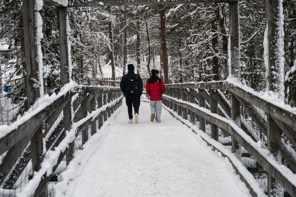A couple walks through a snowy forest bridge in Ranua, Finland, enjoying the winter wonderland.