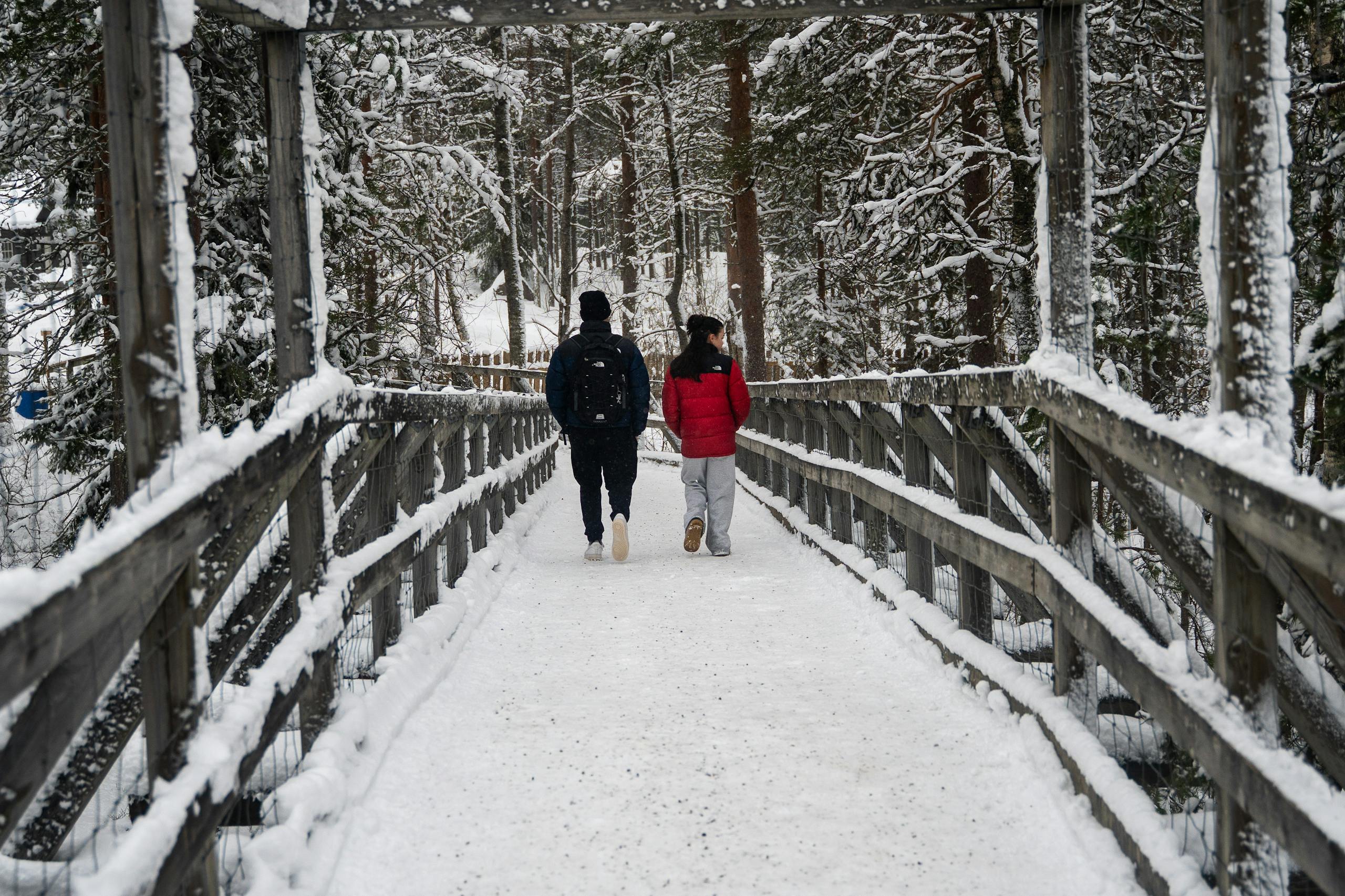 A couple walks through a snowy forest bridge in Ranua, Finland, enjoying the winter wonderland.