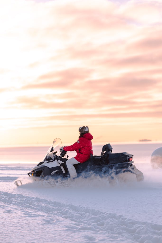 Person riding a snowmobile on a snowy landscape during a beautiful winter sunrise.