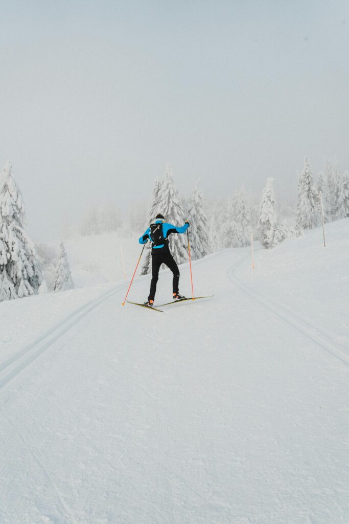 A lone skier glides on a snow-covered trail through a winter landscape with frosty trees. Arctic winter scenery in Lapland covered in fresh snow and frost